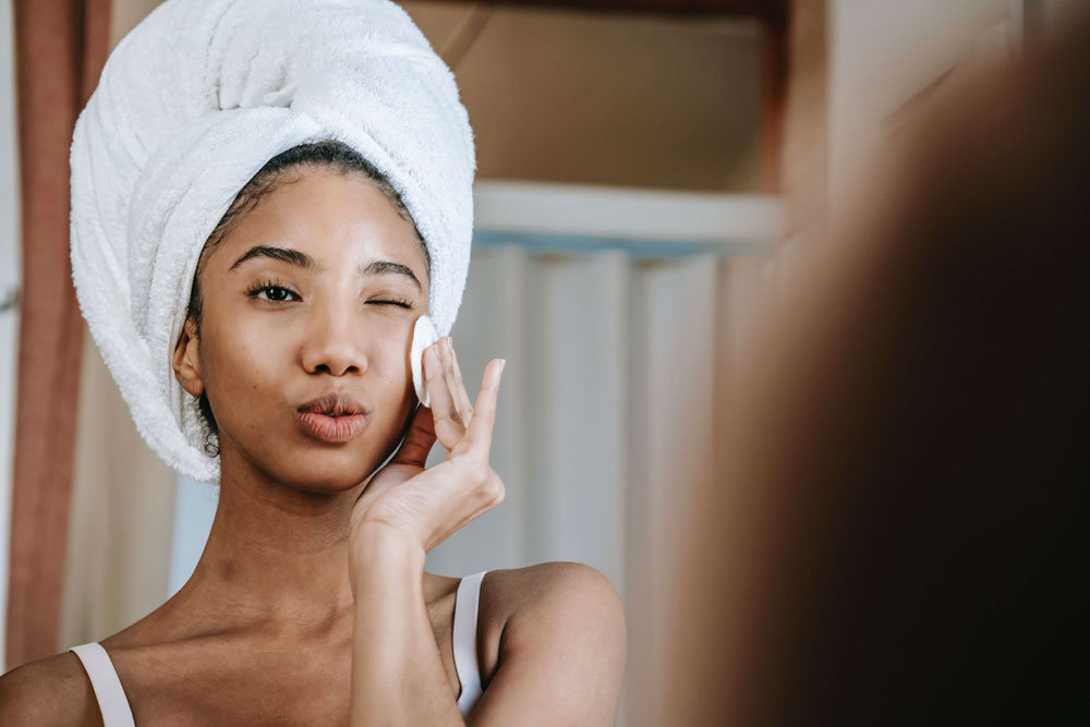 woman with her hair wrapped in a towel, winking and pouting while looking in the mirror and wiping her face