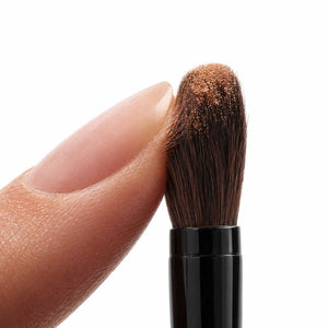 Close-up of the angled precision end of the Palladio Dual Ended Brush being pressed with a fingertip.